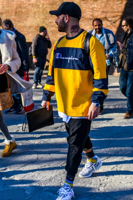 Winter men's oversized winter coordinate outfit with plain black baseball cap, plain yellow Champion sweatshirt, plain black cargo pants, white low-cut Adidas sneakers, and plain black clutch bag/second bag/drawstring.