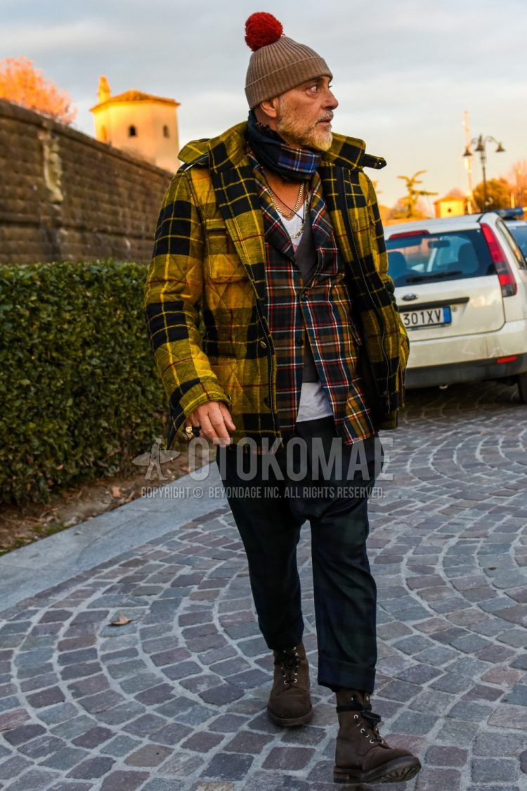 Winter men's outfit with plain brown knit cap, yellow checked quilted jacket, multi-colored checked tailored jacket, plain white t-shirt, plain navy/green slacks, and brown other boots.