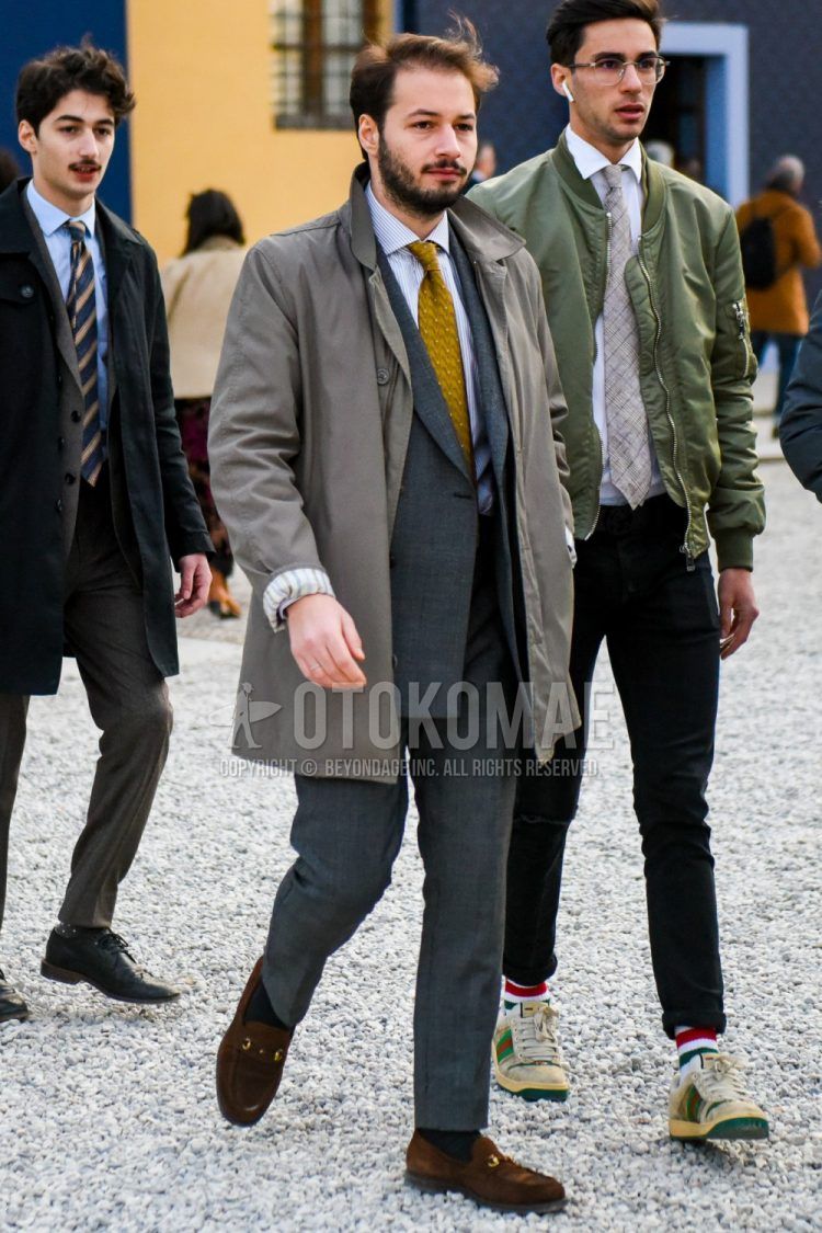 Men's fall/winter outfit with plain gray stainless steel collar coat, white/gray striped shirt, plain navy socks, suede brown bit loafer leather shoes, gray checked suit, and yellow other tie.