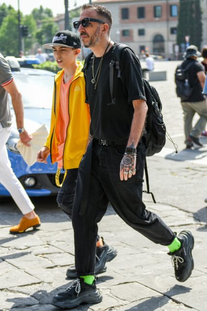 A summer men's oversized summer coordinate outfit with solid black sunglasses, solid black t-shirt, solid black tape belt, solid black cotton pants, solid green socks, Balenciaga black low-cut sneakers, and solid black backpack.