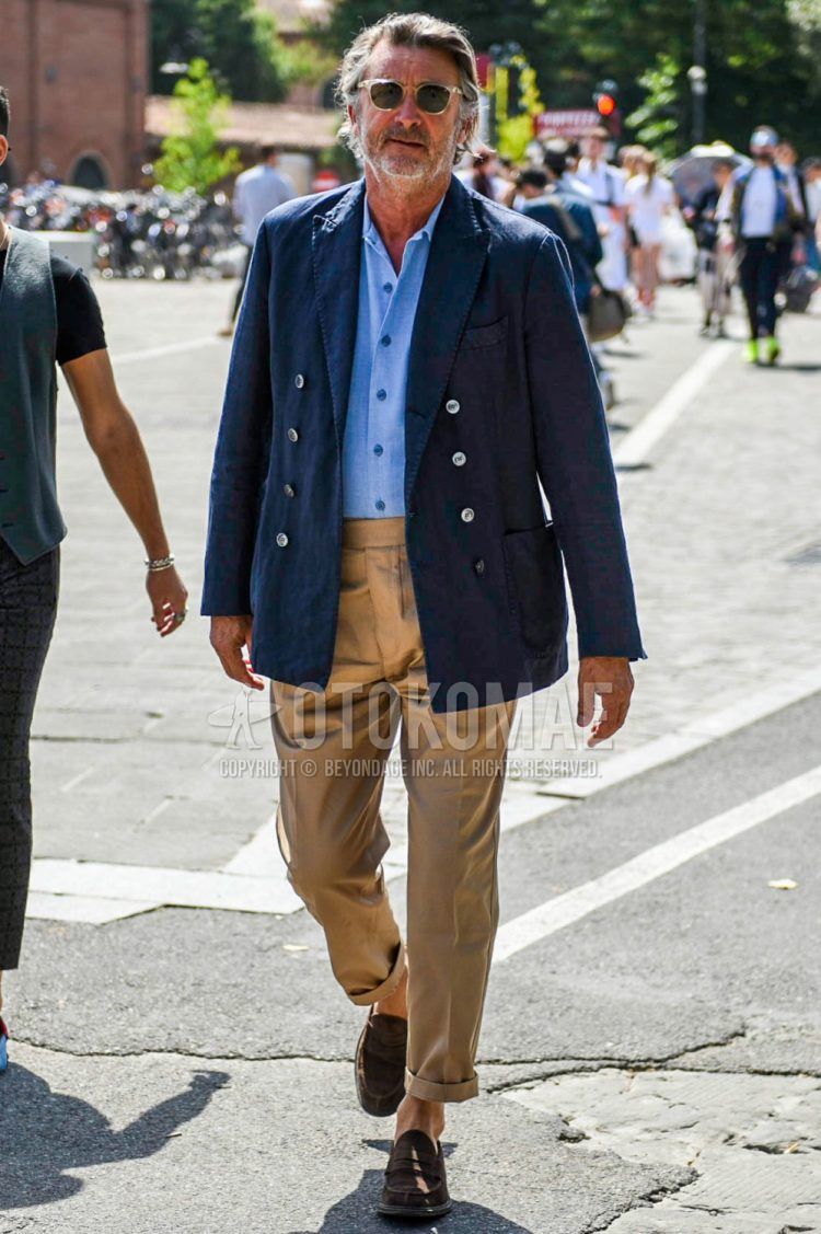 Spring and fall men's coordinate outfit with clear solid color sunglasses, navy solid color tailored jacket, light blue solid color shirt, brown solid color cotton pants, and brown coin loafer leather shoes.