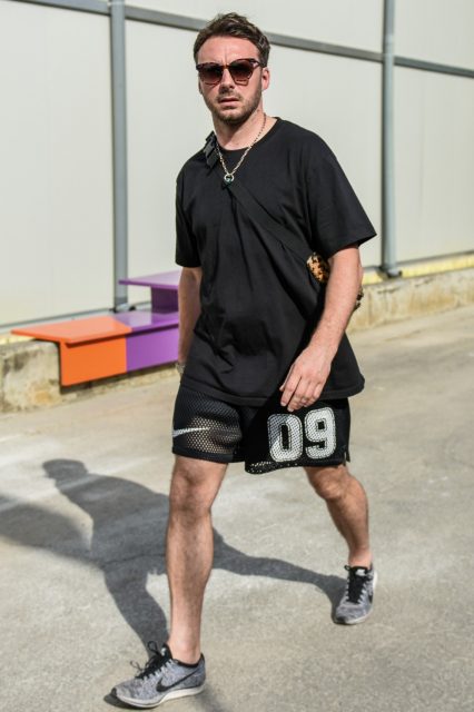 A summer men's oversized coordinate outfit with plain sunglasses, a plain black t-shirt, plain black Nike shorts, and Nike Flyknit Racer gray low-cut sneakers.