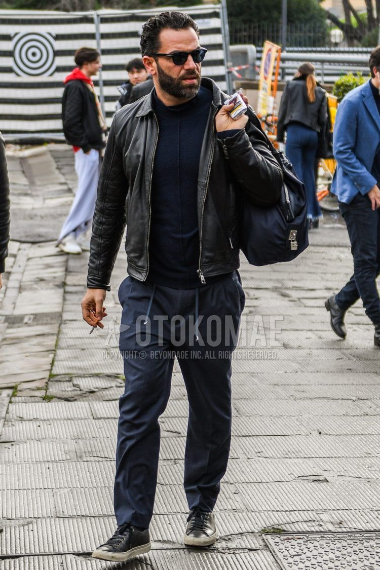 Men's fall/spring/winter outfit with solid color sunglasses, solid color black leather jacket (other than rider's), solid color black sweater, solid color gray easy pants, and black low-cut sneakers.