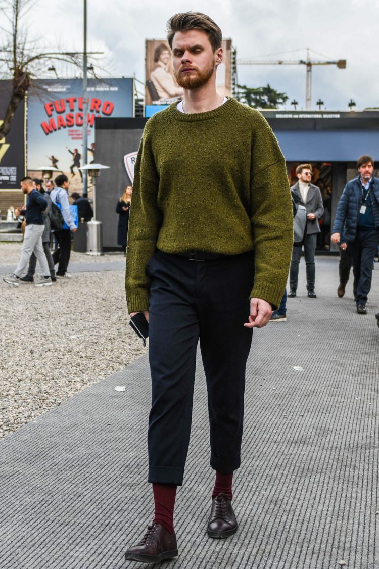 A winter men's oversized coordinate outfit with an olive green solid sweater, dark gray solid slacks, red solid socks, and brown low-cut sneakers.