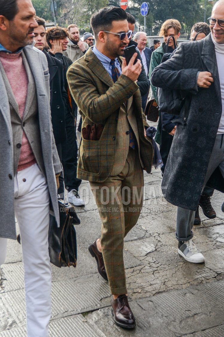 Men's fall/winter outfit with plain sunglasses, olive green checked tailored jacket, white/blue striped shirt, brown u-tip leather shoes, beige checked suit, brown/navy other tie.
