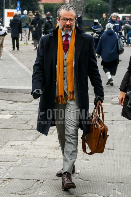Winter men's outfit with plain orange glasses, plain scarf/stall, plain black chester coat, plain light blue shirt, brown other boots, plain brown briefcase/handbag, plain gray three-piece suit, and red dot tie.
