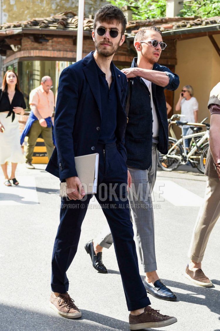 A spring, summer, and fall men's coordinate outfit with plain gold sunglasses, plain navy polo shirt, brown low-cut sneakers, and plain navy suit.