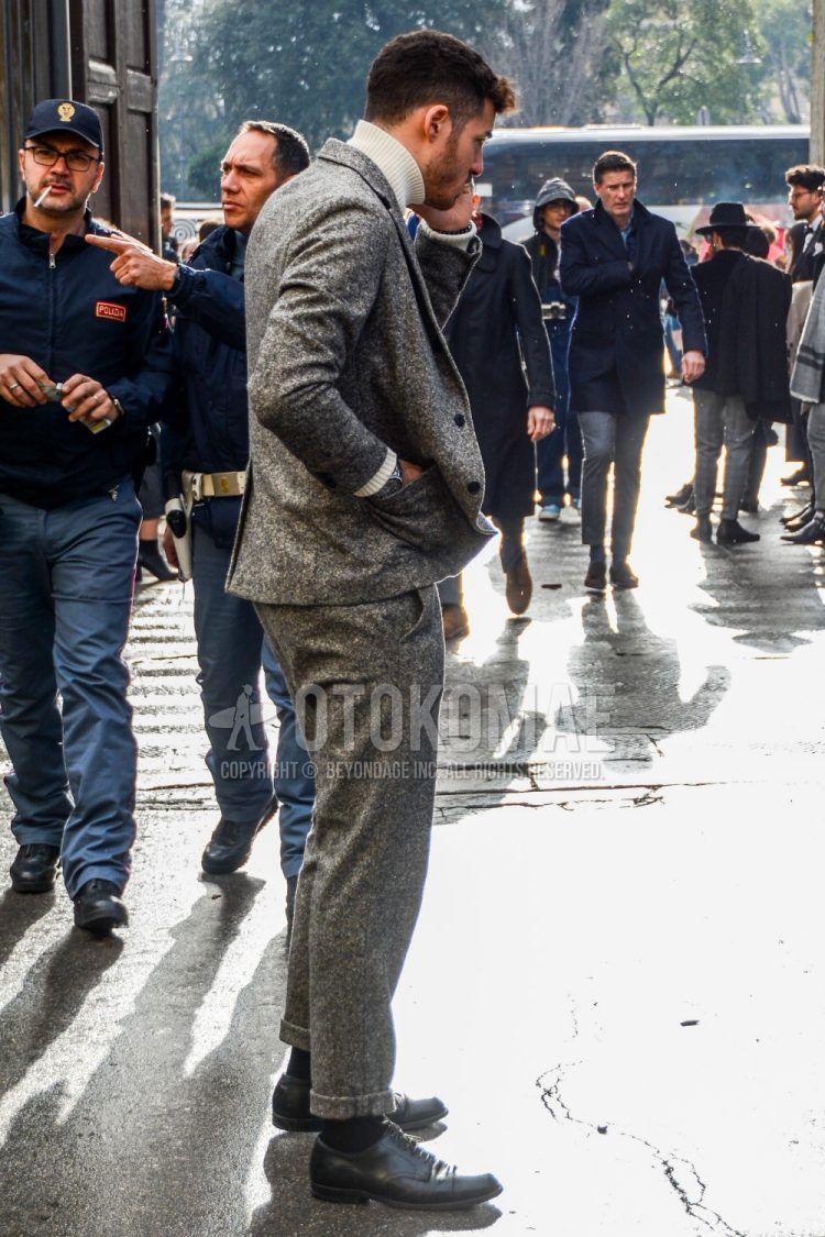 A plain white turtleneck knit, plain black socks, black straight tip leather shoes, and a plain gray suit for a men's fall outfit.