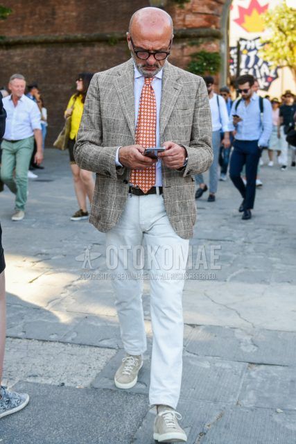 Men's coordinate and outfit with black/brown tortoiseshell glasses, gray checked tailored jacket, plain white shirt, plain brown leather belt, plain white chinos, plain ankle pants, beige low-cut sneakers and orange tie.