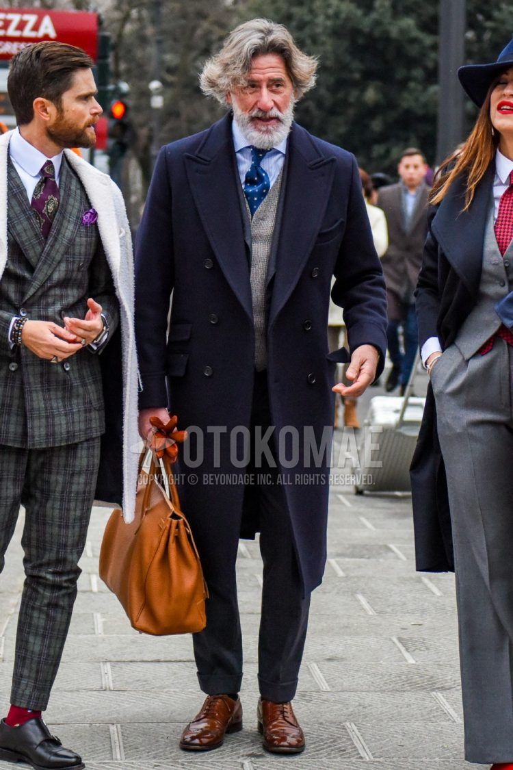 Men's fall/winter outfit with plain navy chester coat, blue striped shirt, gray checked gilet, brown wingtip leather shoes, solid beige briefcase/handbag, solid gray suit, and blue dot tie.