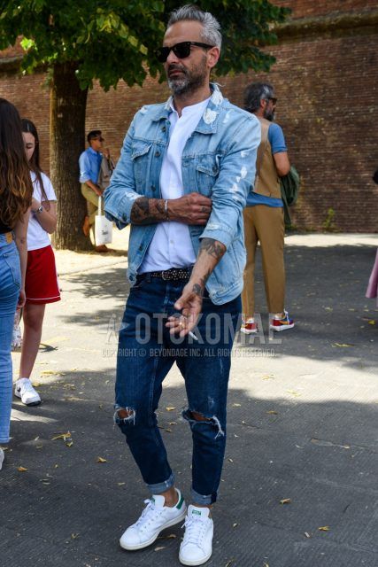 Men's coordinate and outfit with square solid black sunglasses, solid light blue denim jacket, solid white shirt, solid black leather belt, solid blue damaged jeans, and Adidas Stan Smith white low-cut sneakers.