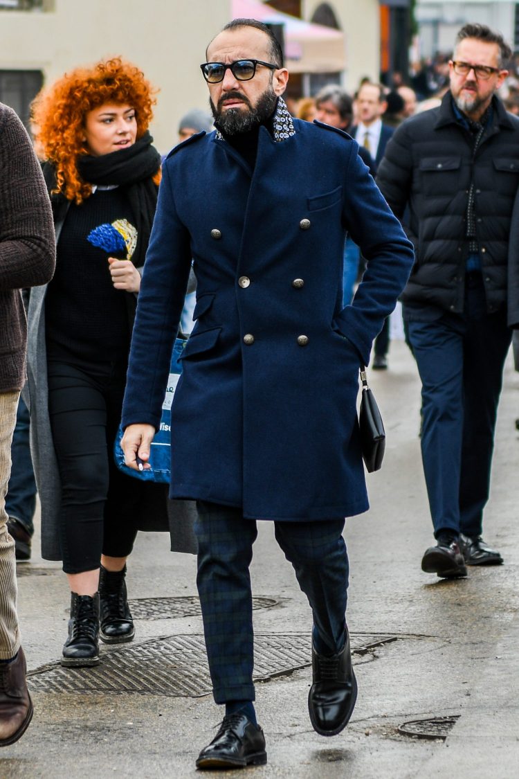 A men's fall/winter outfit with plain sunglasses, a plain navy chester coat, black/green checked slacks, plain black socks, and black plain toe leather shoes.