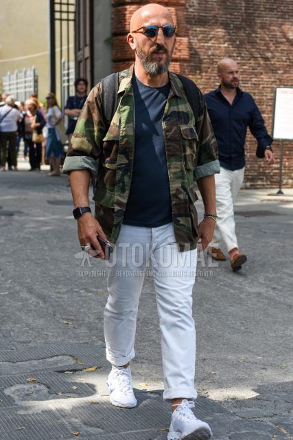 Men's coordinate and outfit with plain brown sunglasses, green camouflage shirt jacket, plain green M-65, plain navy t-shirt, plain white cotton pants, and white low-cut Nike sneakers.