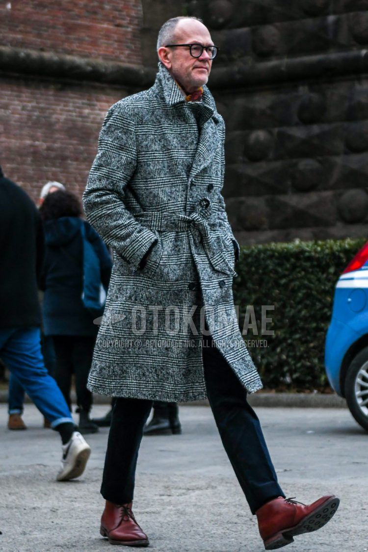 Winter men's outfit with plain glasses, red solid color scarf/stall, gray checked belted coat, navy solid color slacks, and brown chukka boots.