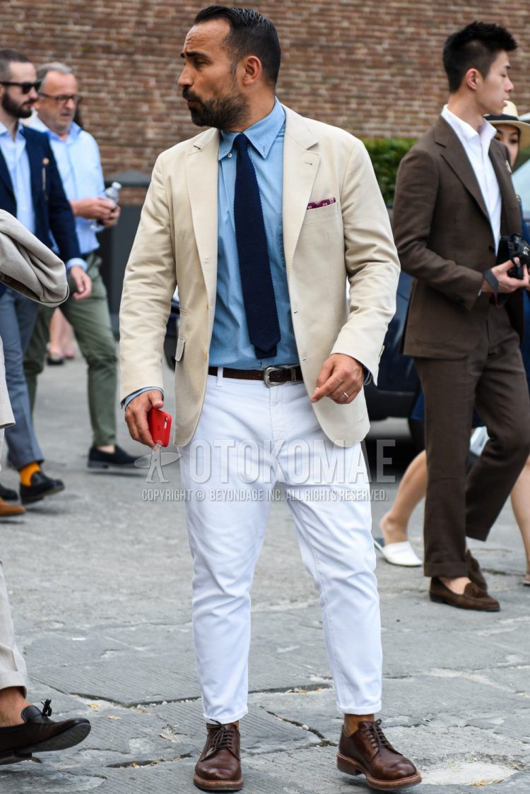 Spring, summer, and fall men's outfit with a solid beige tailored jacket, solid blue shirt, solid brown leather belt, solid white cotton pants, brown plain toe leather shoes, and solid navy tie.