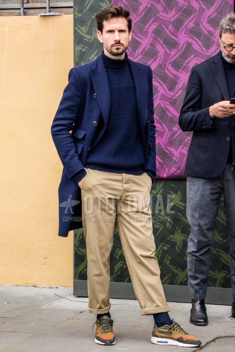 Fall/winter men's outfit with plain navy chester coat, plain navy turtleneck knit, multi-colored plain chinos, plain gray socks, and Nike Air Max olive green/orange low-cut sneakers.