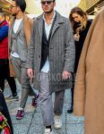 A men's fall/winter outfit with plain sunglasses, a gray herringbone stainless steel coat, a gray/black checked tailored jacket, a plain white shirt, plain gray cotton pants, plain black socks, and white low-cut sneakers.