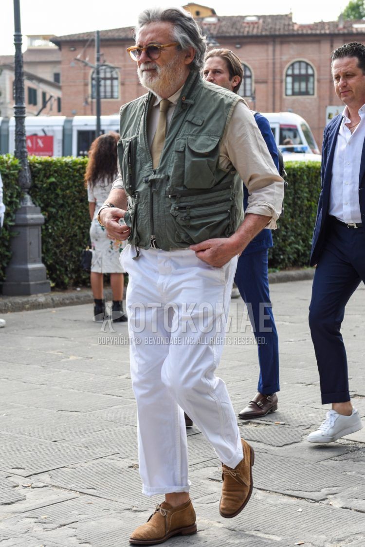 A spring/summer/fall men's coordinate outfit with solid color others, solid color yellow glasses, solid color beige shirt, solid color olive green gilet, solid color white cotton pants, beige chukka boots, and solid color beige tie.