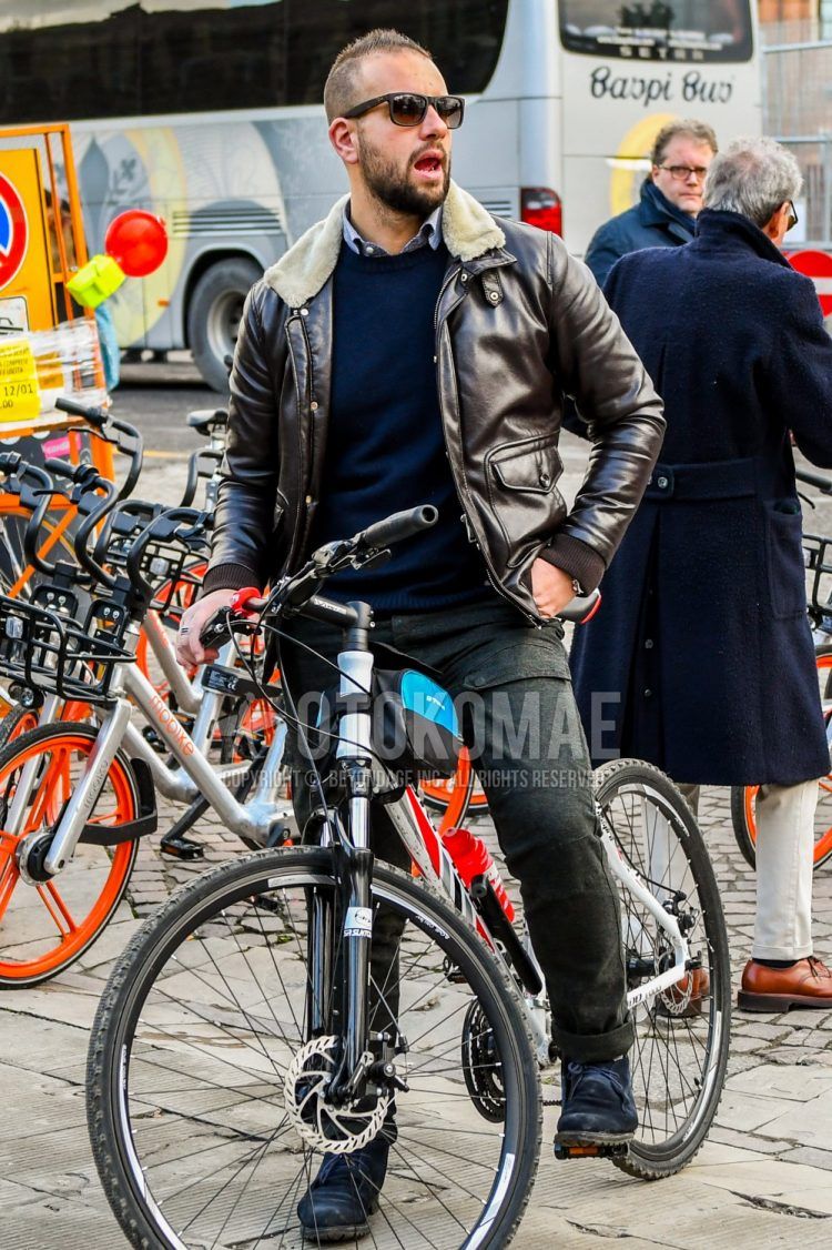 A men's fall/winter outfit with solid color sunglasses, solid color brown leather jacket (not riders), solid color navy sweater, solid color gray shirt, solid color gray cargo pants, solid color slacks, and black chukka boots.