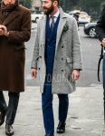 Men's fall/winter outfit with plain gray Ulster coat, plain white shirt, black monk shoes leather shoes, blue checked suit, and gray other tie.