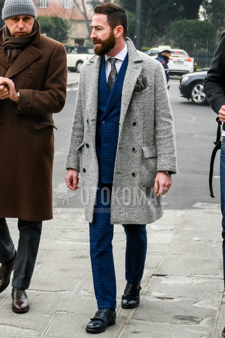 Men's fall/winter outfit with plain gray Ulster coat, plain white shirt, black monk shoes leather shoes, blue checked suit, and gray other tie.
