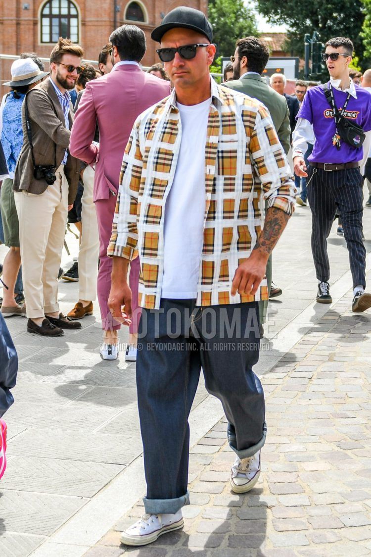 Men's coordinate and outfit with plain black baseball cap, plain black Wellington sunglasses, beige checked shirt, plain white t-shirt, plain navy denim/jeans, and Converse All Star white high-cut sneakers.