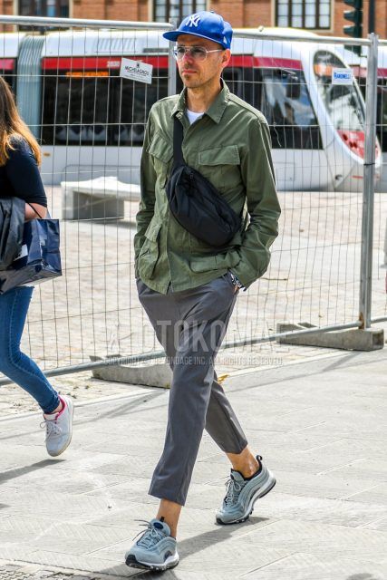 Men's outfit/clothing with plain blue baseball cap from New Era, plain sunglasses, plain olive green M-65, plain white t-shirt, plain grey ankle pants, grey low-cut sneakers from Nike, and plain black briefcase/handbag.