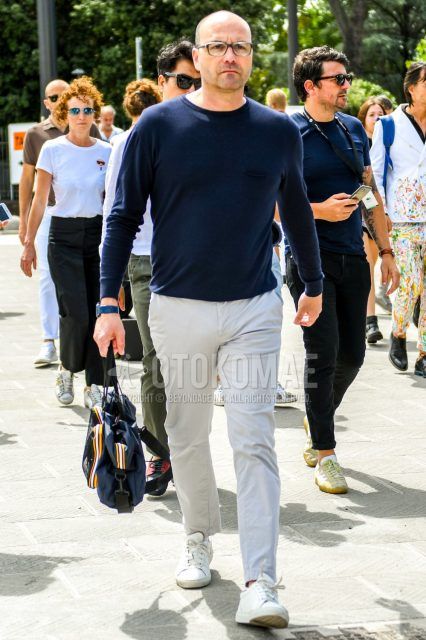 Men's coordinate and outfit with plain black glasses, plain navy long T, plain beige chinos, white low-cut sneakers, and plain navy briefcase/handbag.