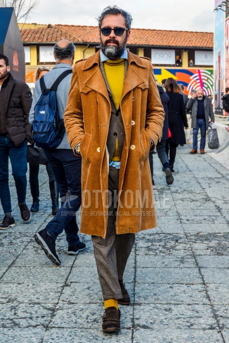 Fall/winter men's outfit with solid color sunglasses, solid color brown trench coat, solid color yellow sweater, solid color light blue denim/chambray shirt, brown monk shoes leather shoes, suede shoes leather shoes, and brown checked suit.