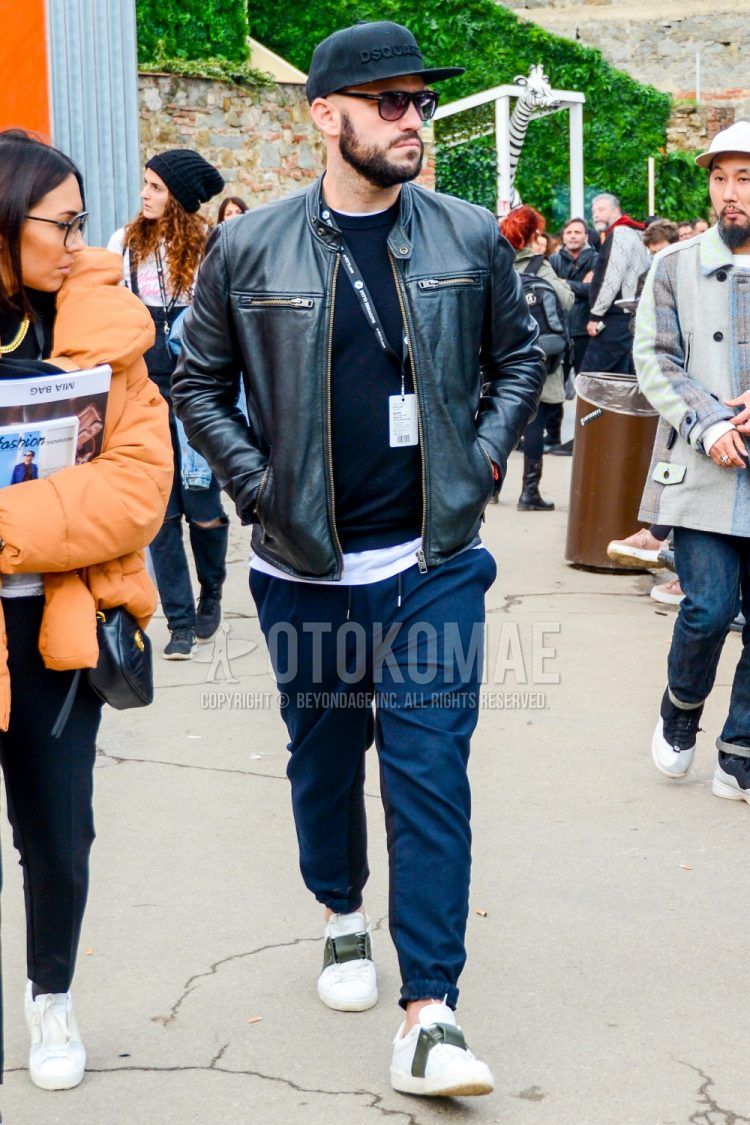 A solid color baseball cap, solid color sunglasses, solid color black rider's jacket, solid color black sweater, solid color white t-shirt, solid color gray easy pants, solid color jogger pants/ribbed pants, and Valentino white low-cut sneakers for men's fall/winter outfits.