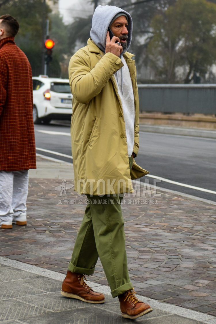 A men's fall/winter outfit with a solid beige down jacket, solid gray hoodie, solid olive green chinos, and brown work boots.
