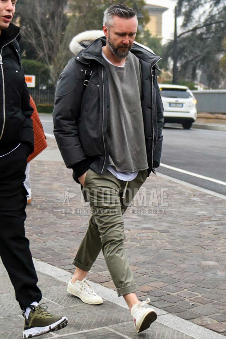 A men's fall/winter outfit with a plain gray down jacket, plain olive green/gray sweatshirt, plain white t-shirt, plain beige/olive green chinos, and Play Comme des Garcons Converse white low-cut sneakers.