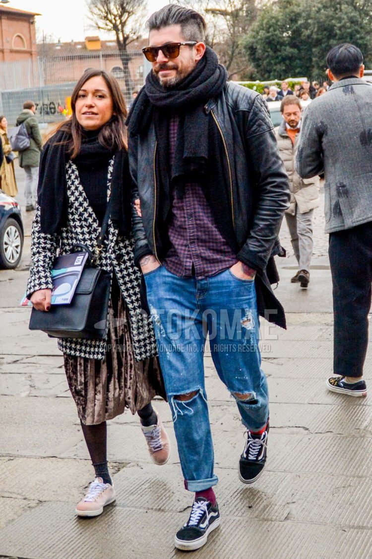 Wearing a men's fall/winter outfit with solid color sunglasses, solid color gray scarf/stall, solid color black rider's jacket, red checked shirt, solid color blue damaged jeans, solid color red socks, and Vans Old School black low-cut sneakers.