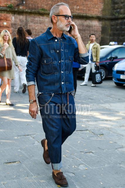 Men's coordinate and outfit with solid black sunglasses, solid blue denim jacket, blue/brown striped t-shirt, solid brown leather belt, solid blue denim/jeans, and suede brown tassel loafer leather shoes.