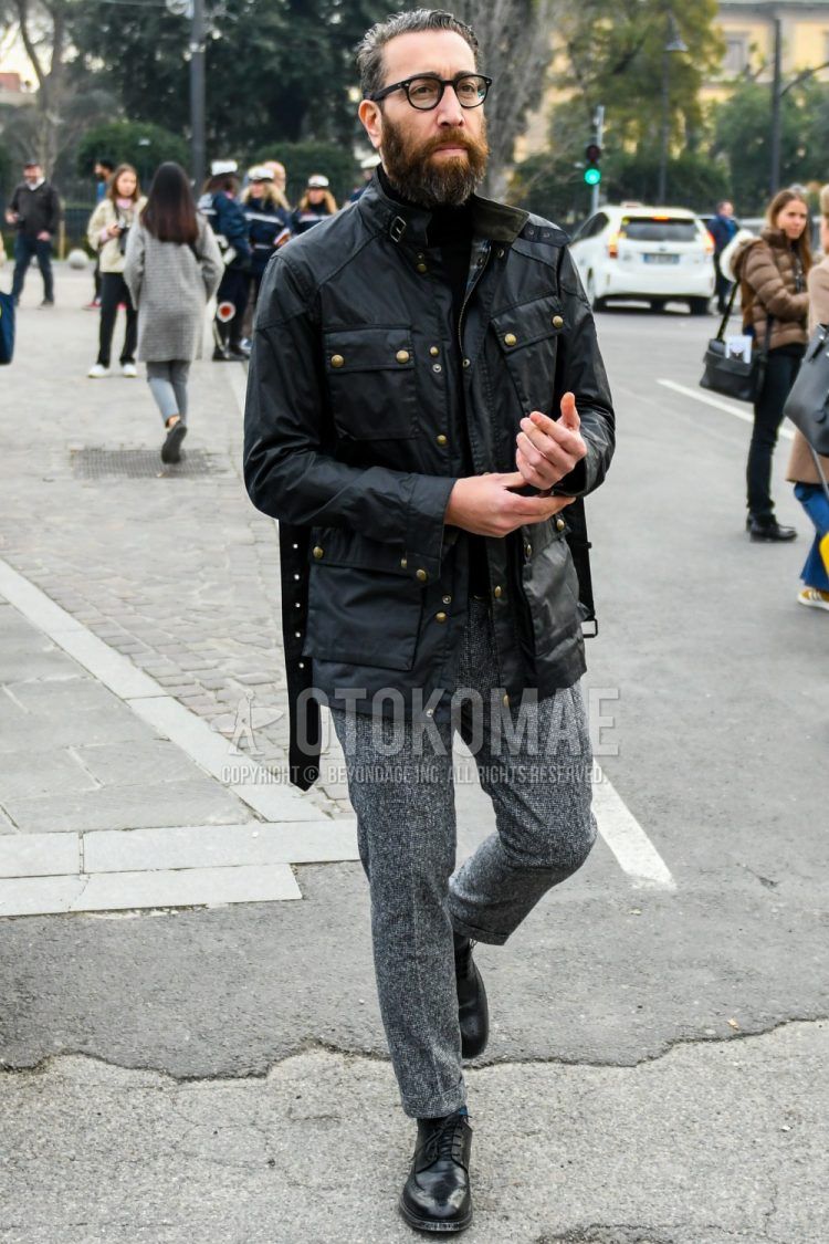 A winter/fall men's outfit with plain glasses, a plain black Belstaff rider's jacket, a plain black turtleneck knit, plain gray slacks, and black wingtip leather shoes.