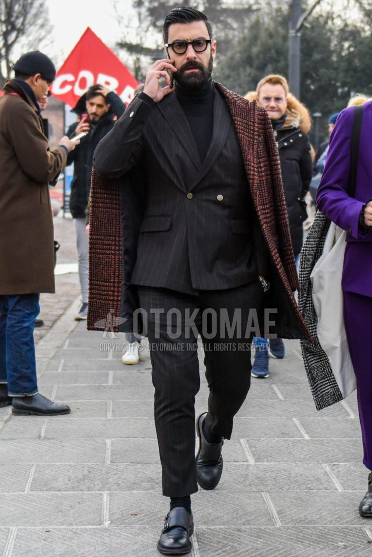 Men's fall/winter coordinate outfit with plain glasses, black/orange check chester coat, plain black turtleneck knit, plain black socks, black monk shoe leather shoes, and black striped suit.