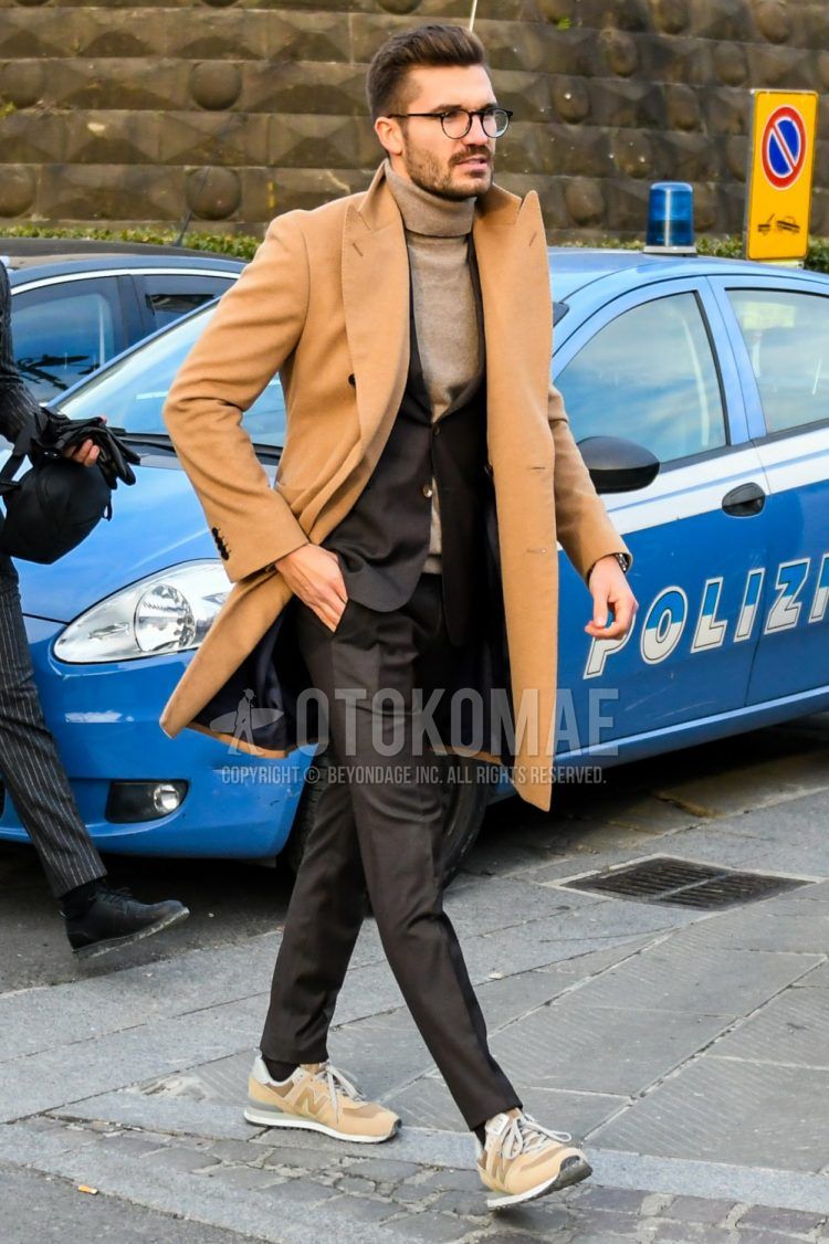 A winter men's outfit of plain glasses, plain brown chester coat, plain brown turtleneck knit, plain brown socks, New Balance brown low-cut sneakers, and a plain brown suit.