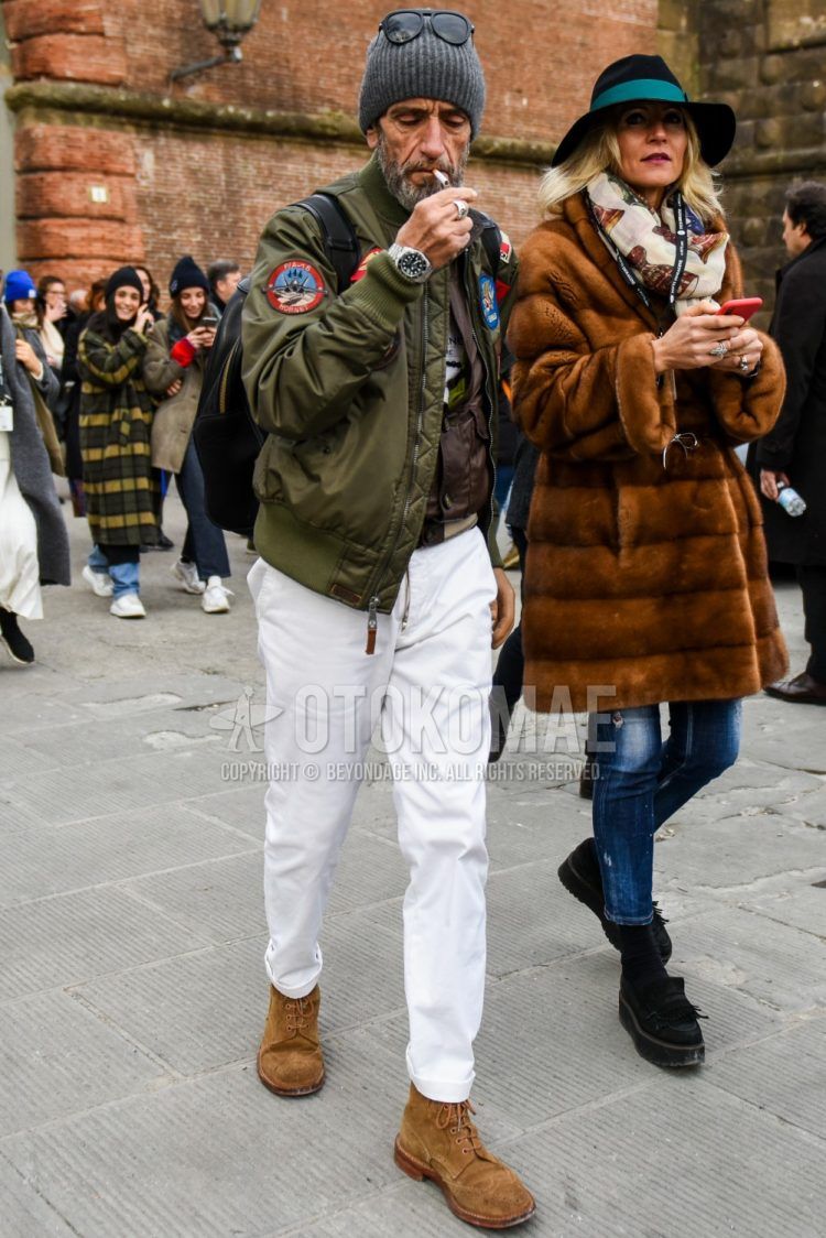 Fall/spring men's coordinate outfit with plain gray knit cap, plain sunglasses, plain olive green MA-1, white graphic t-shirt, plain white cotton pants, and blue and other boots.