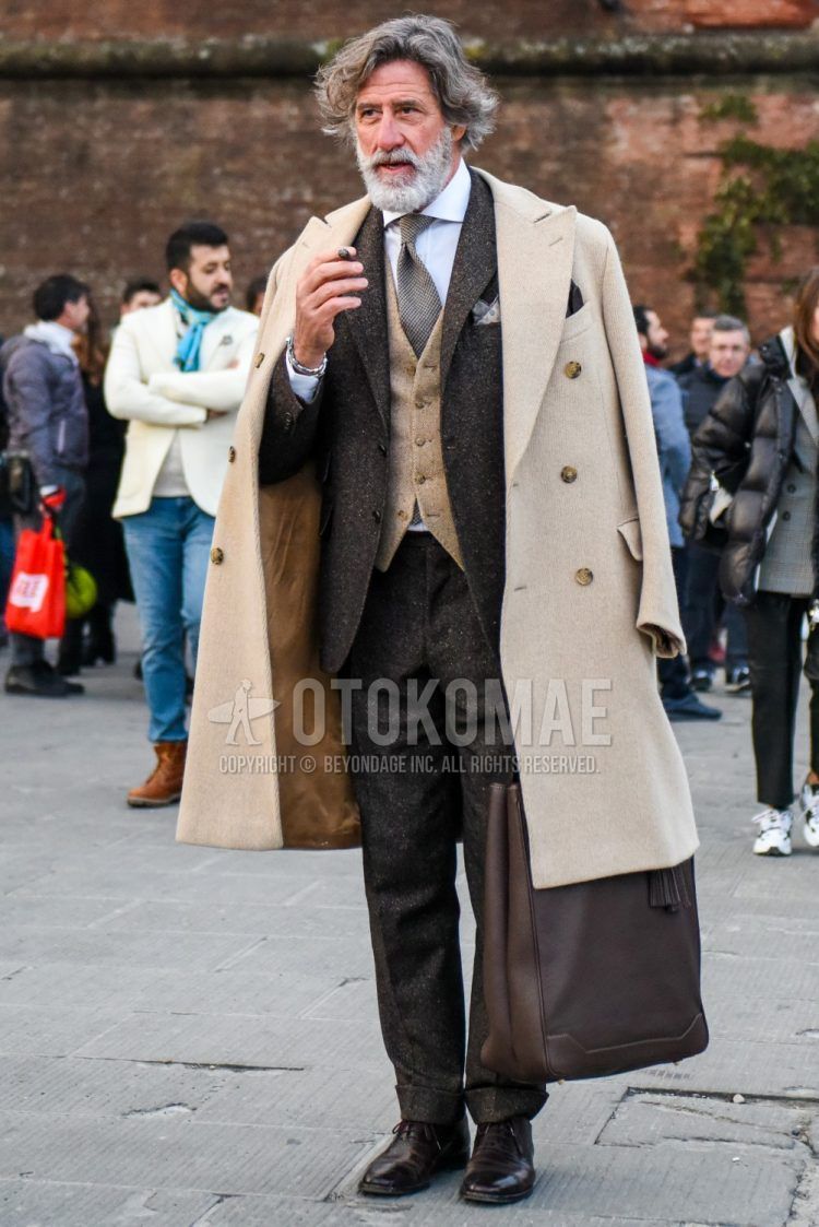 Winter men's outfit with plain beige chester coat, plain beige gilet, plain white shirt, brown straight tip leather shoes, plain brown tote bag, plain brown suit and brown other tie.