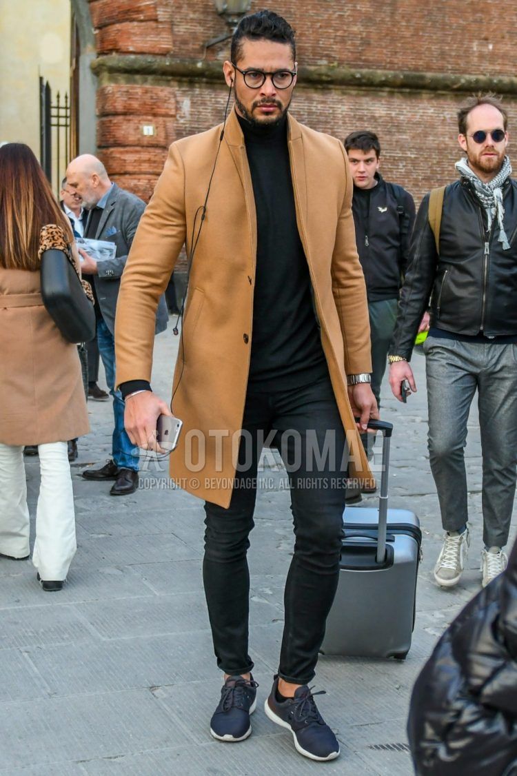 Wearing plain black glasses, plain beige chester coat, plain black turtleneck knit, plain black denim/jeans, and dark gray low-cut sneakers in a men's fall/winter outfit.