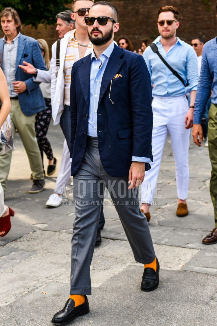 Men's coordinate and outfit with plain black sunglasses, plain navy tailored jacket, plain light blue shirt, plain gray slacks, plain orange socks, and black coin loafer leather shoes.