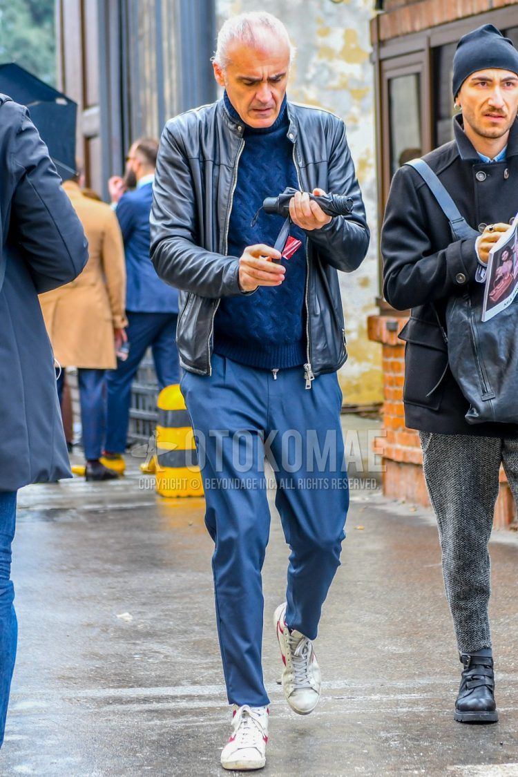 A men's fall/winter outfit with a plain black rider's jacket, a plain navy turtleneck knit, plain gray slacks, and white high-cut sneakers.