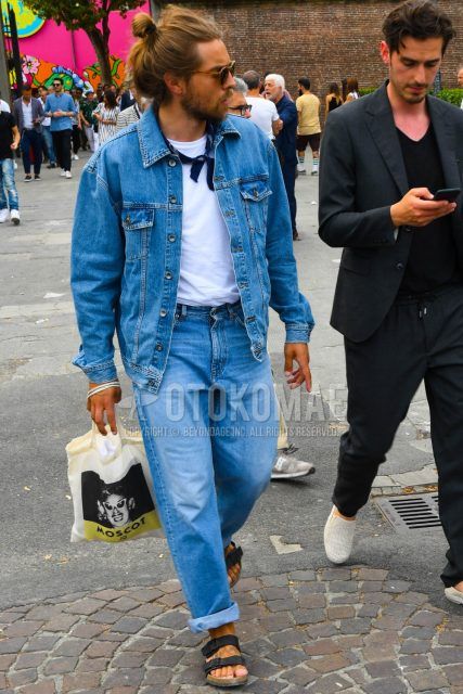 A men's spring/summer/fall outfit with solid color sunglasses, solid color blue denim jacket, solid color white t-shirt, solid color blue denim/jeans, and leather sandals.
