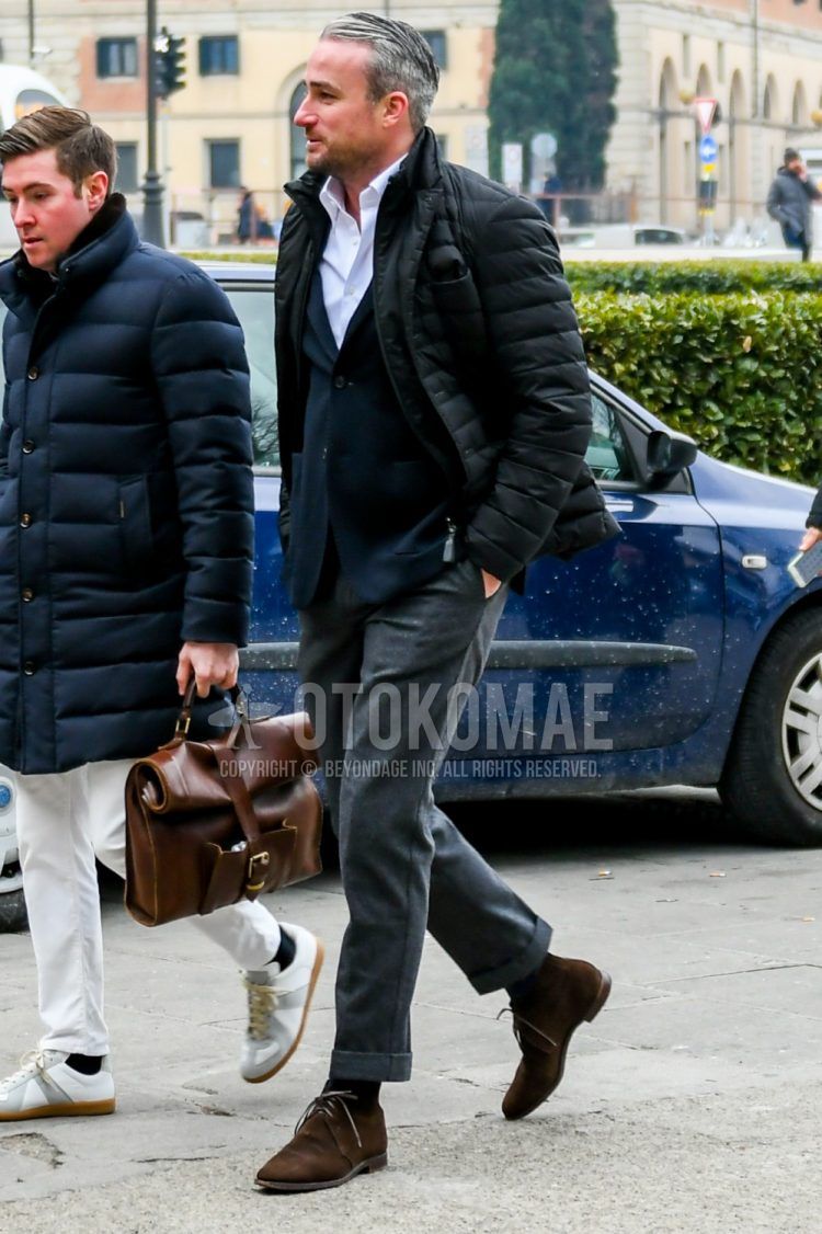 A men's fall/winter outfit with a plain black down jacket, plain white shirt, plain navy tailored jacket, plain gray slacks, plain black socks, and suede brown chukka boots.