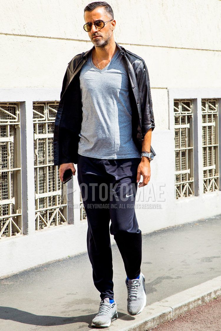 Spring and fall men's coordinate outfit with solid color sunglasses, solid color black rider's jacket, solid color gray t-shirt, solid color black Nike sweatpants, and gray low-cut sneakers.