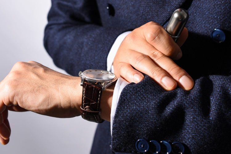 香水アトマイザーを手に持ちながら時計を確認するスーツ姿の男性