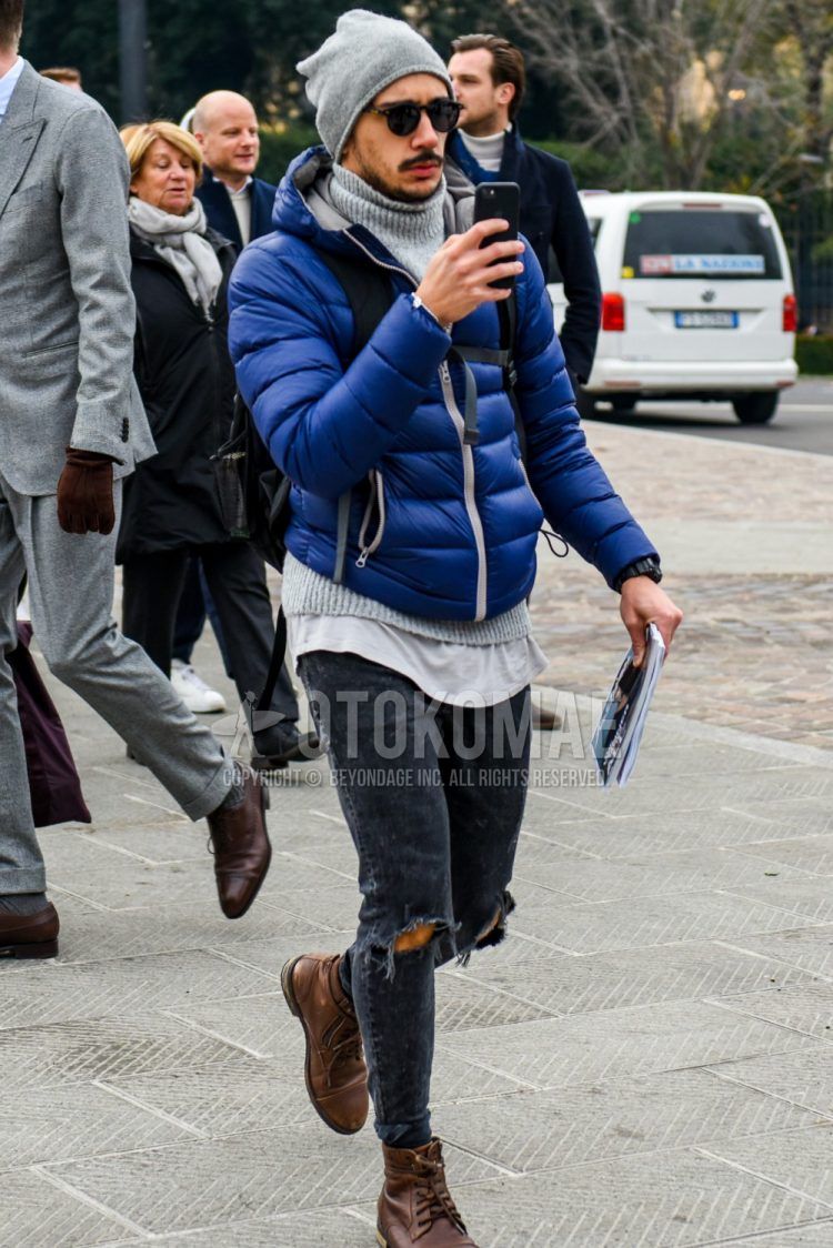 Men's coordinate and outfit with plain gray knit cap, plain sunglasses, plain blue down jacket, plain gray sweater, plain dark gray damaged jeans, and brown work boots.