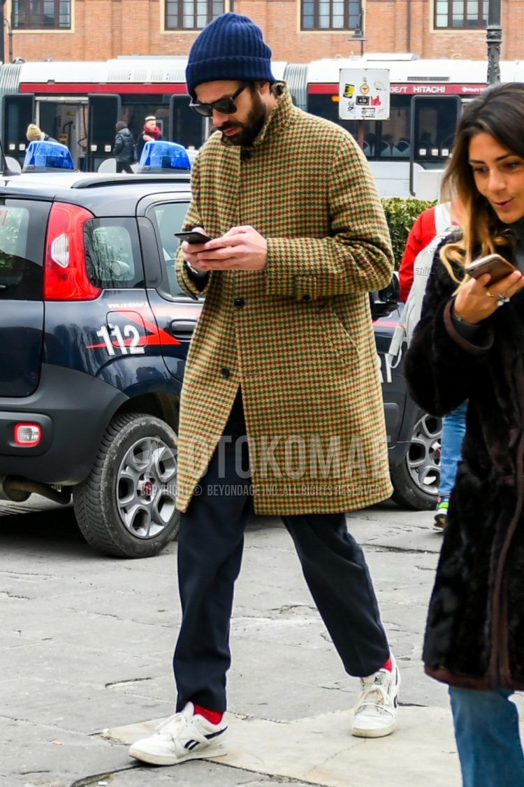 Men's coordinate and outfit with solid navy knit cap, solid black sunglasses, beige checked stainless steel coat, solid gray slacks, solid red socks, and white low-cut Reebok sneakers.