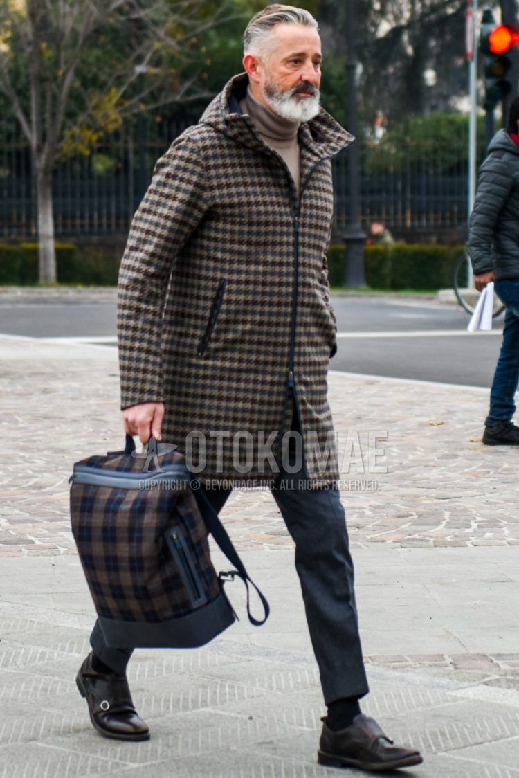 Men's coordinate and outfit with brown checked hooded coat, solid beige turtleneck knit, solid gray slacks, brown monk shoes leather shoes, and brown checked backpack.