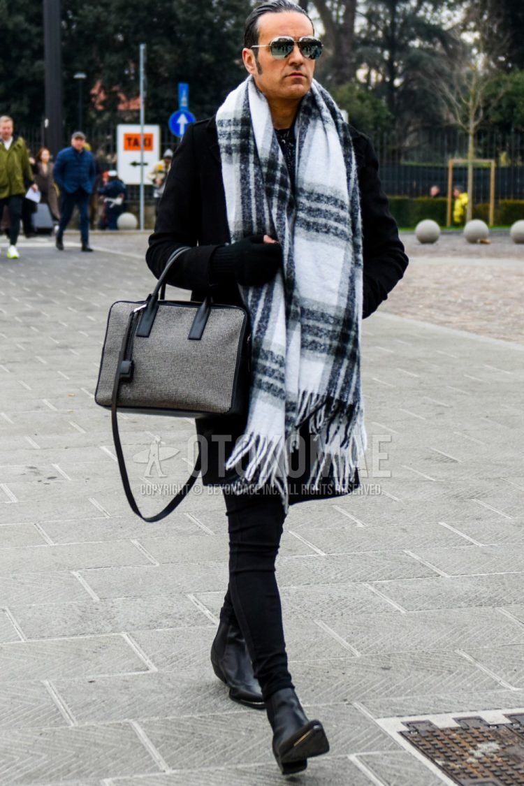 Men's coordinate and outfit with plain silver sunglasses, white checked scarf/stall, plain black Ulster coat, plain black skinny pants, black boots, and plain gray briefcase/handbag.